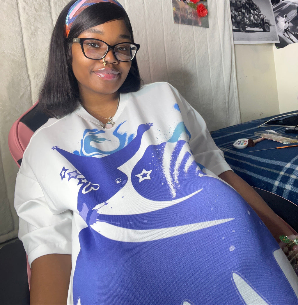 A woman wearing a white t-shirt with a blue and white shark graphic print, sitting in a room with posters on the wall.